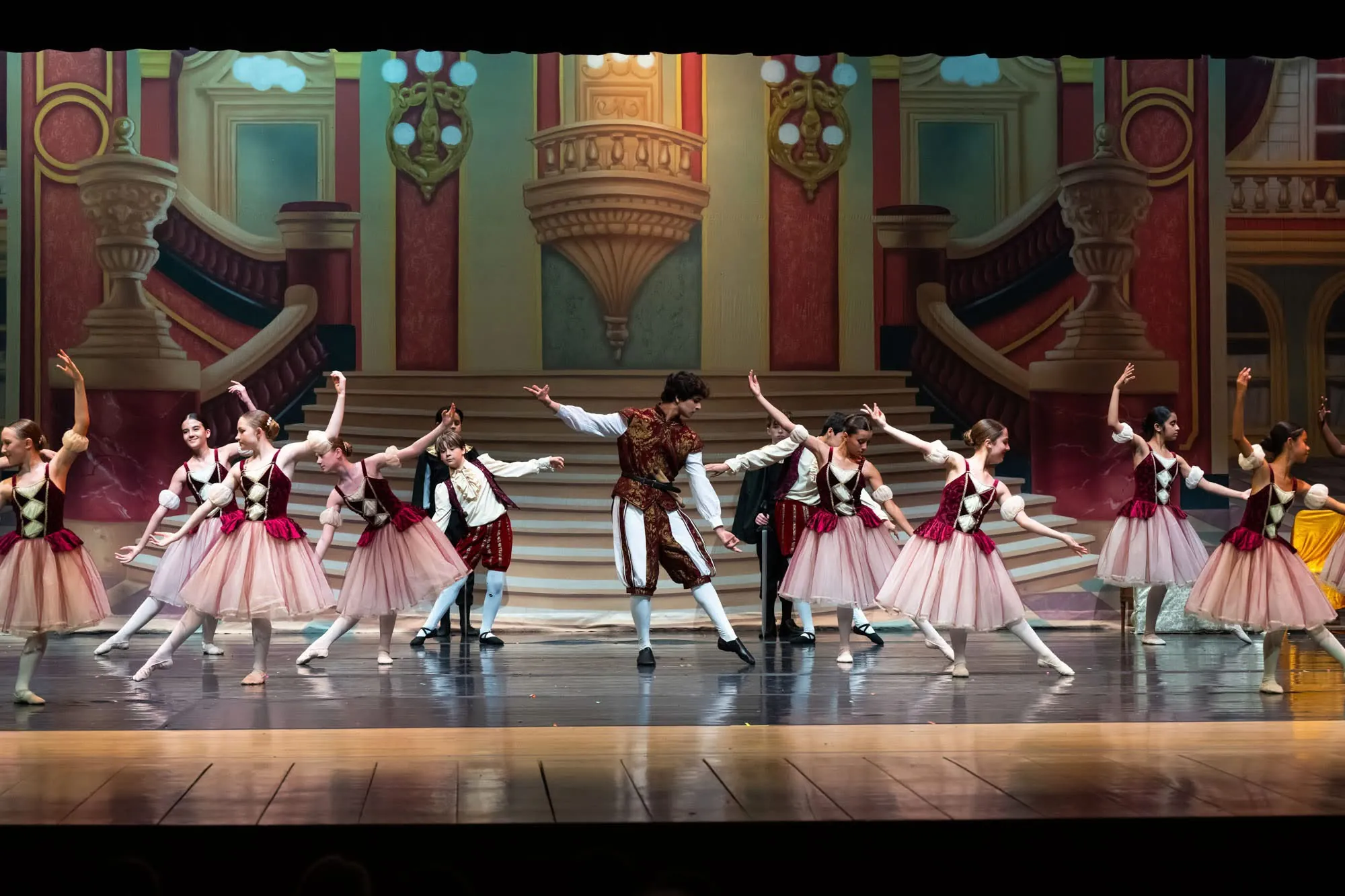Dancers in red, white and pink folk costumes dancing on a palace stage set